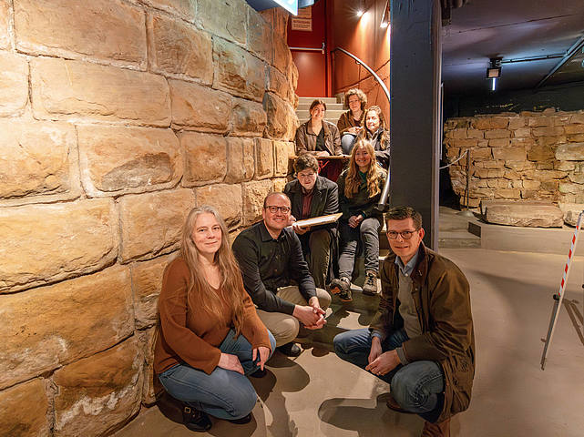Die Gruppe sitzt am Fuß der Ruine des Roten Turms im Historischen Museum Saar.