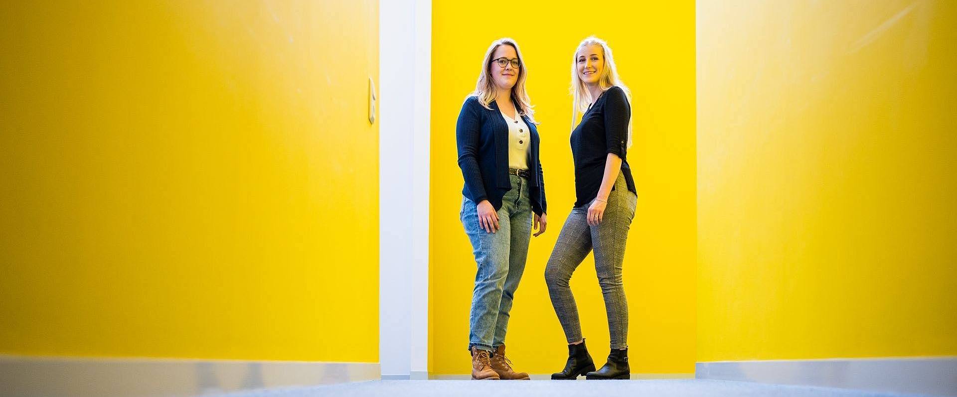 Zwei Studentinnen stehen vor einer gelben Wand