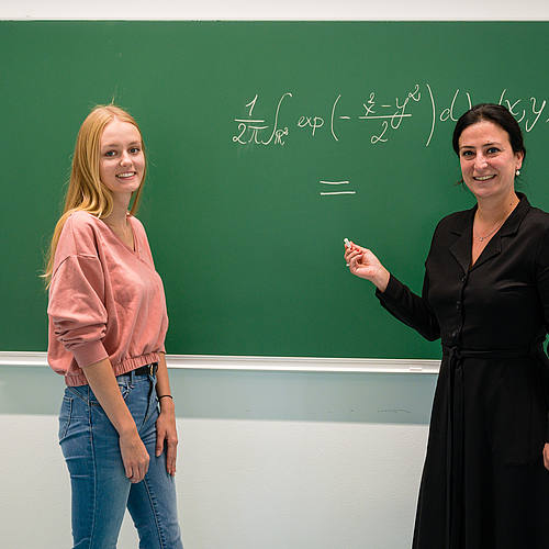 zwei Frauen vor einer Schiefertafel, auf der eine mathematische Formel geschrieben steht