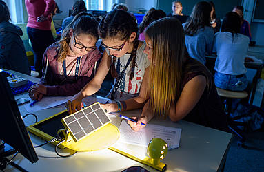 Drei Mädchen beugen sich über ein Solarmodul.