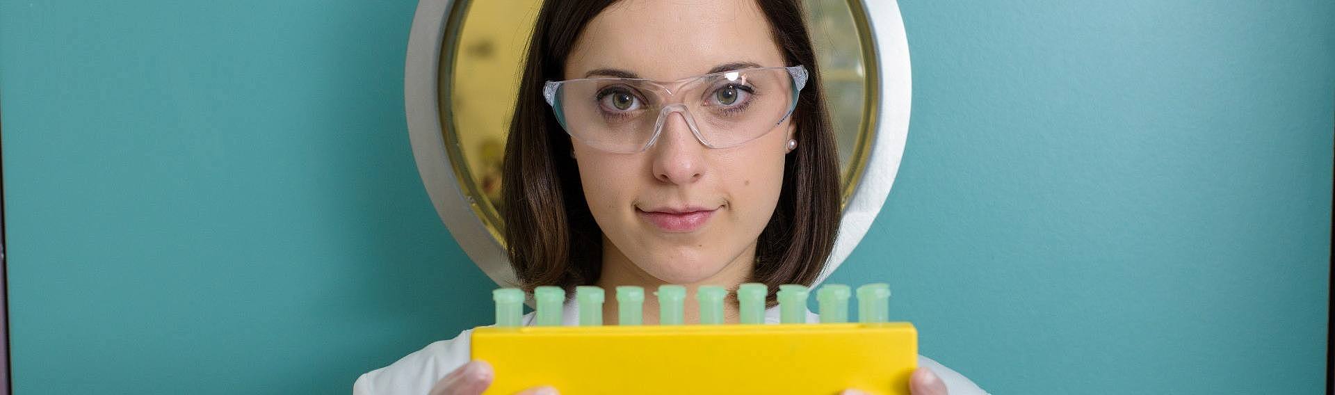 Studentin hält im Labor einen Behälter mit Proben in der Hand