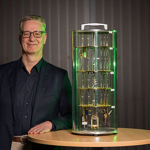 Wolfgang Maaß steht neben einem Modell eines Quantencomputers.
