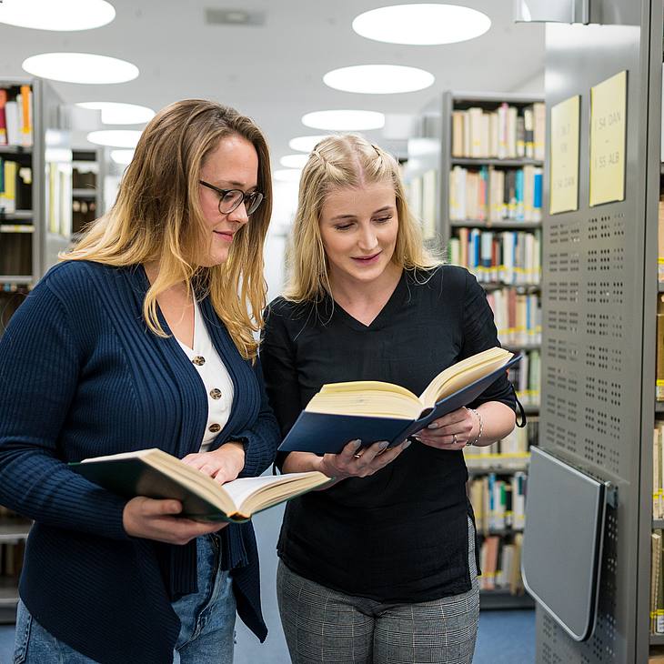 Zwei Studentinnen blicken in Bücher in der Uni-Bibliothek