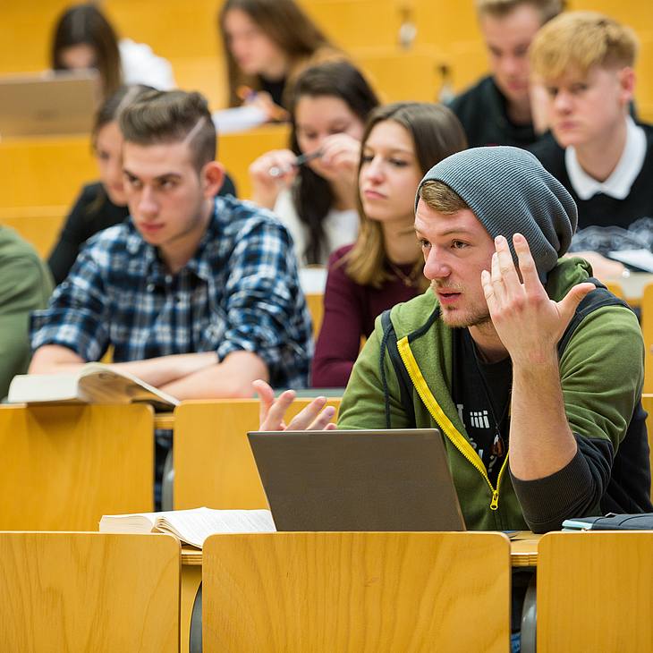 Studenten im Hörsaal, ein Student hebt argumentierend seine Hand