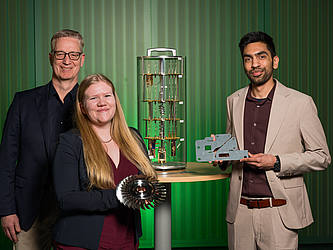 Die drei Wissenschaftler stehen um ein Modell eines Quantencomputers.