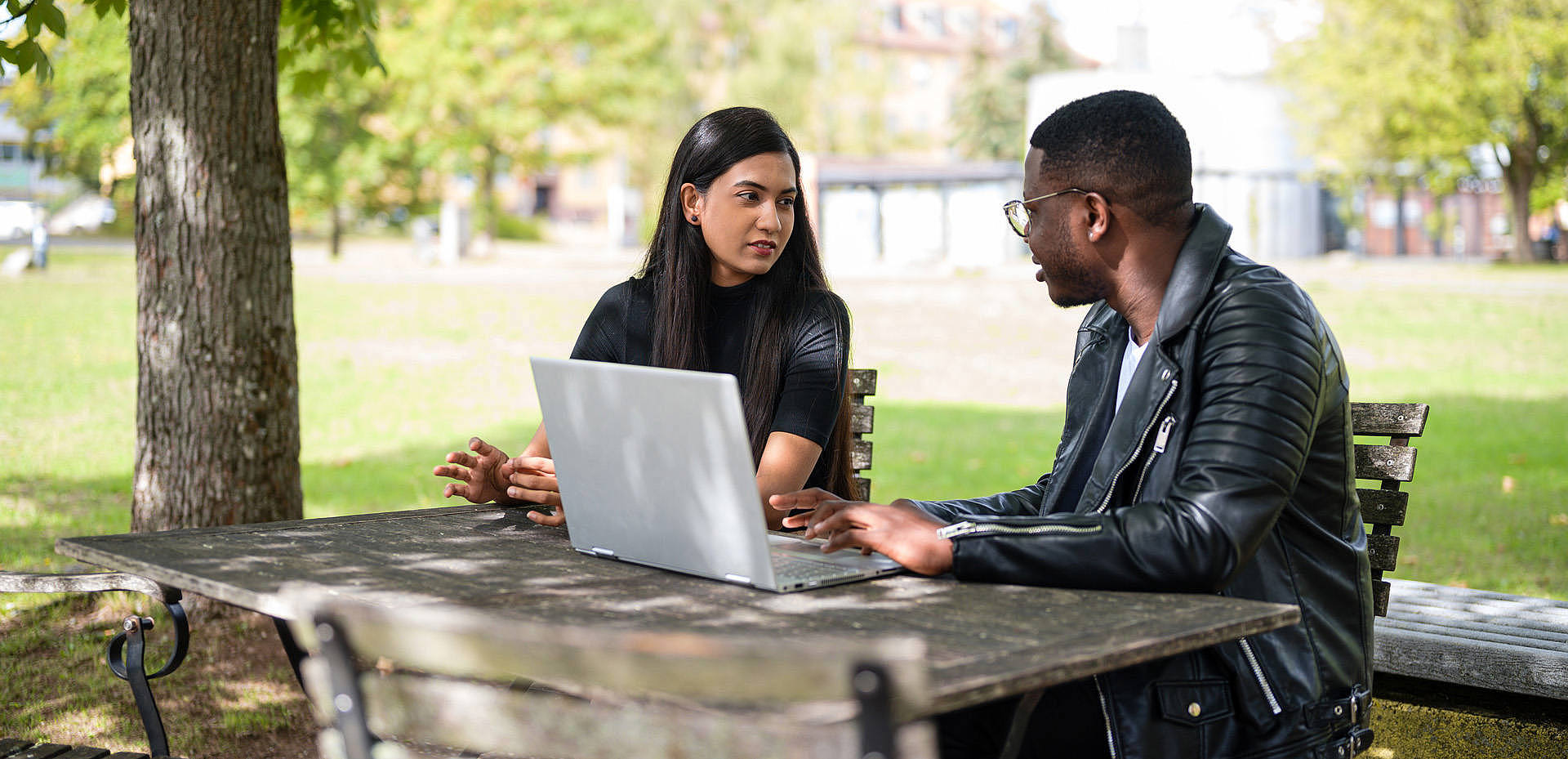 Junge Frau und junger Mann mit Laptop an einem Tisch auf der Campus-Wiese
