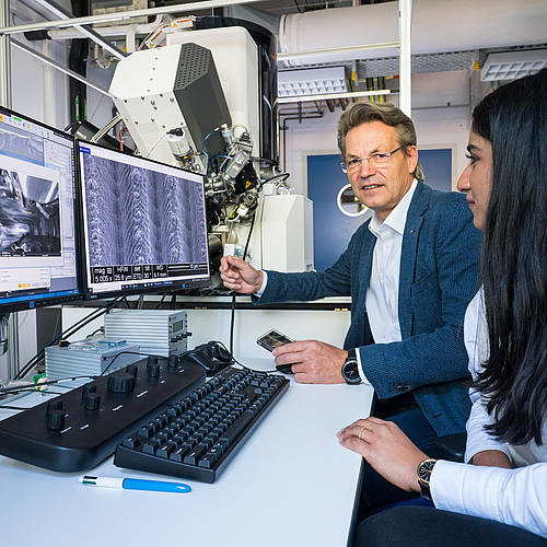 Professor Frank Mücklich und Doktorandin Aisha Ahmed betrachten im Labor mikroskopische Aufnahmen von Oberflächen auf Computerbildschirmen.
