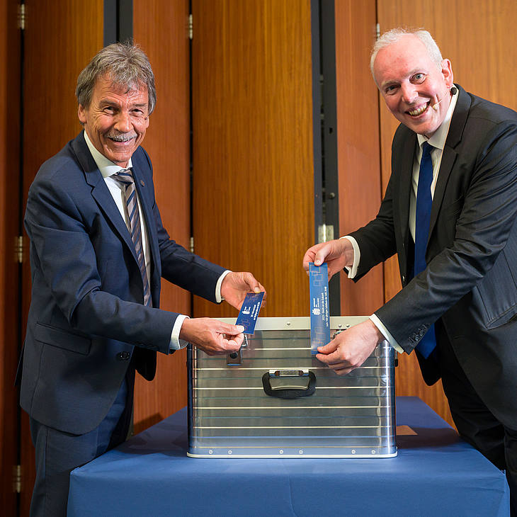 Universitätspräsident Prof. Dr. Manfred Schmitt und Finanzminister Jakob von Weizsäcker versiegeln mit Aufklebern die Zeitkapsel (ein Aluminium-Koffer)