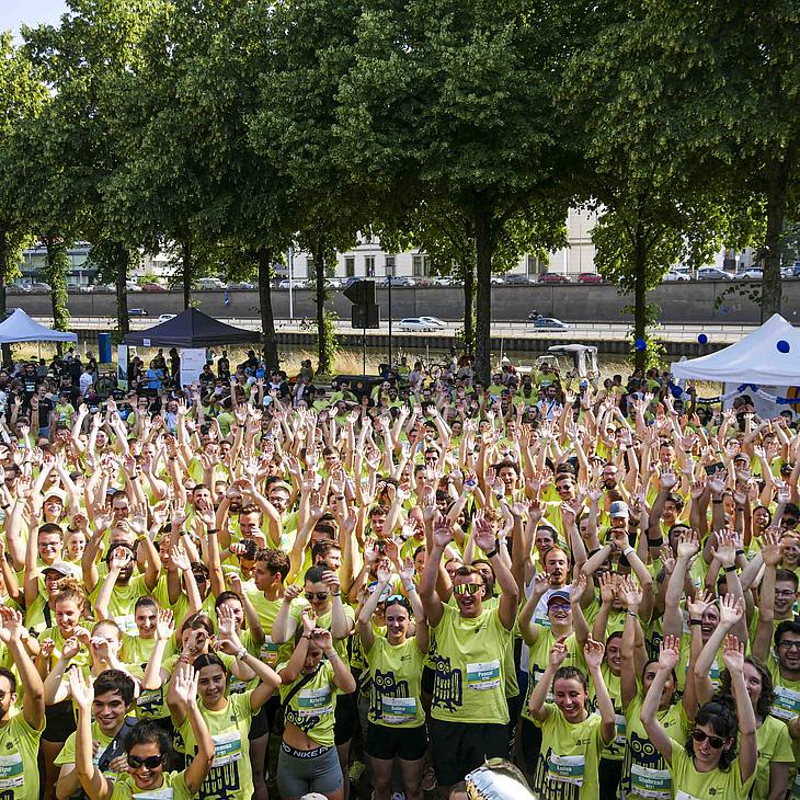 viele Läuferinnen und Läufer in gelb-grünen Universitäts-T-Shirts reißen jubelnd die Arme hoch