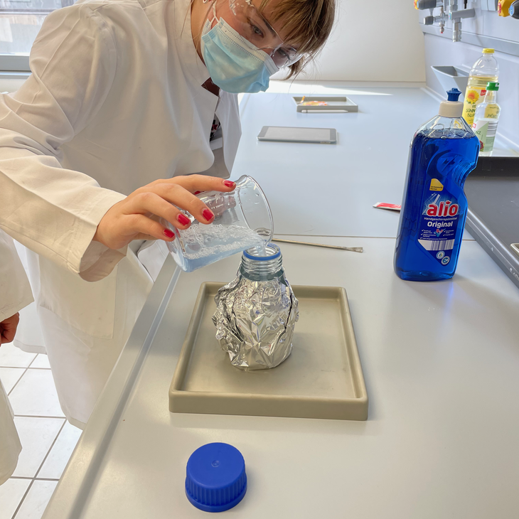 Eine Teilnehmerin des Probestudiums arbeitet im Labor. Hier kippt sie gerade eine Flüssigkeit aus einem Becherglas in eine mit Alu-Folie umwickelte Flasche. 