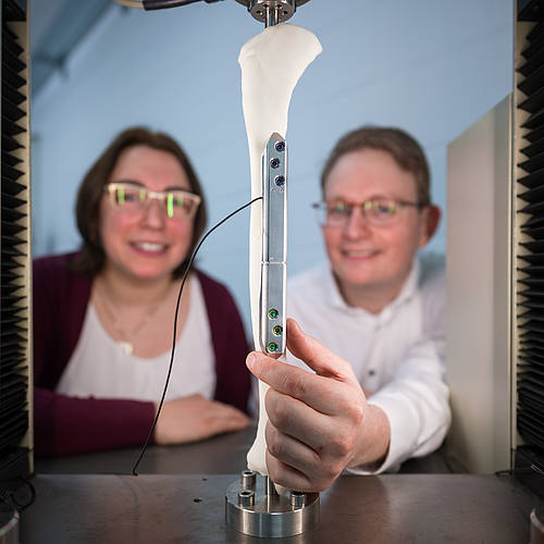Die Forscherin und der Forscher zeigen einen Knochen, auf dem eine silberne Implantat-Schiene angebracht ist.