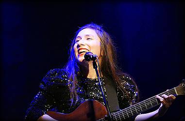 Junge Frau mit Gitarre auf einer Bühne mit schwarzem Hintergrund