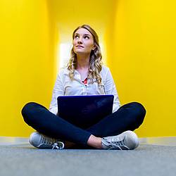 Studentin im Schneidersitz vor gelbem Hintergrund