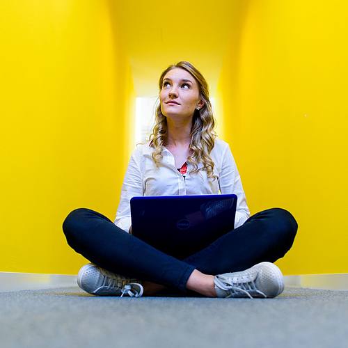 Studentin im Schneidersitz vor gelbem Hintergrund