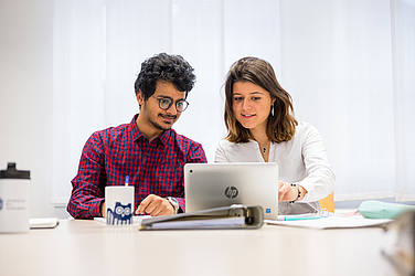 zwei Studierende vor einem aufgeklappten Laptop