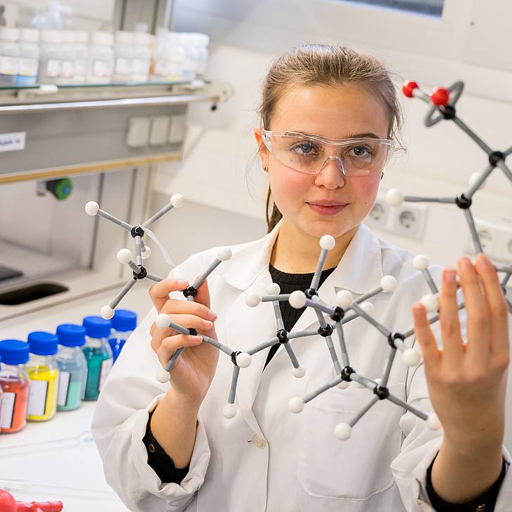 Studentin im Chemielabor hält Molekülmodell in der Hand