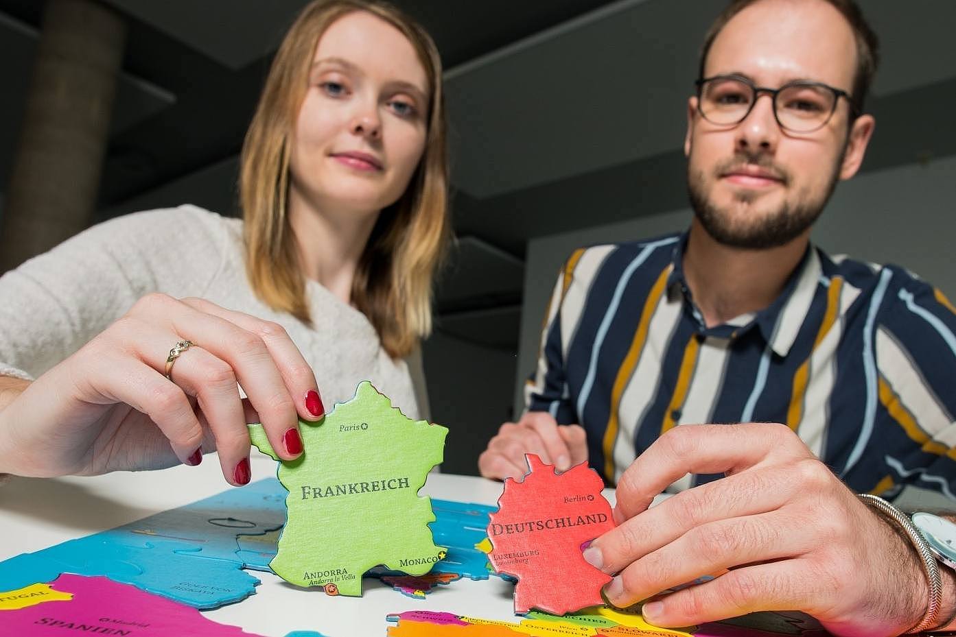 Studentin und Student zeigen zwei Puzzleteile mit dem Umriss von Frankreich und Deutschland