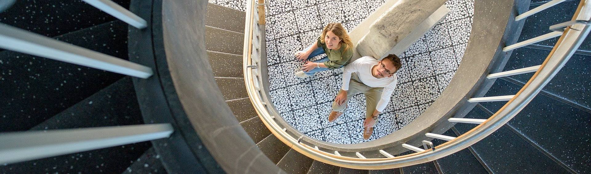 Aufsicht auf zwei Studierende am Fuß einer Wendeltreppe