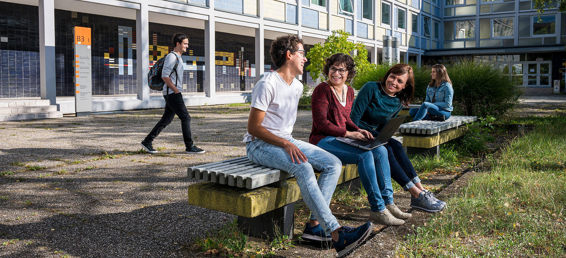 Studierende sitzen auf Bänken vor einem Universitätsgebäude
