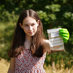 Junge Probesammlerin steht auf einer Wiese und hält eine Plastiktüte mit Bodenprobe in der Hand