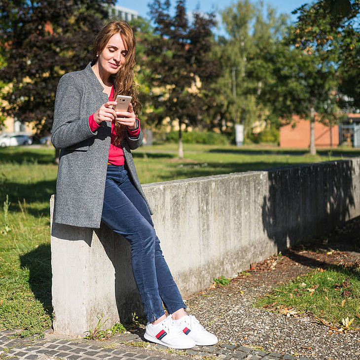 Studentin steht mit Handy vor der Campuswiese