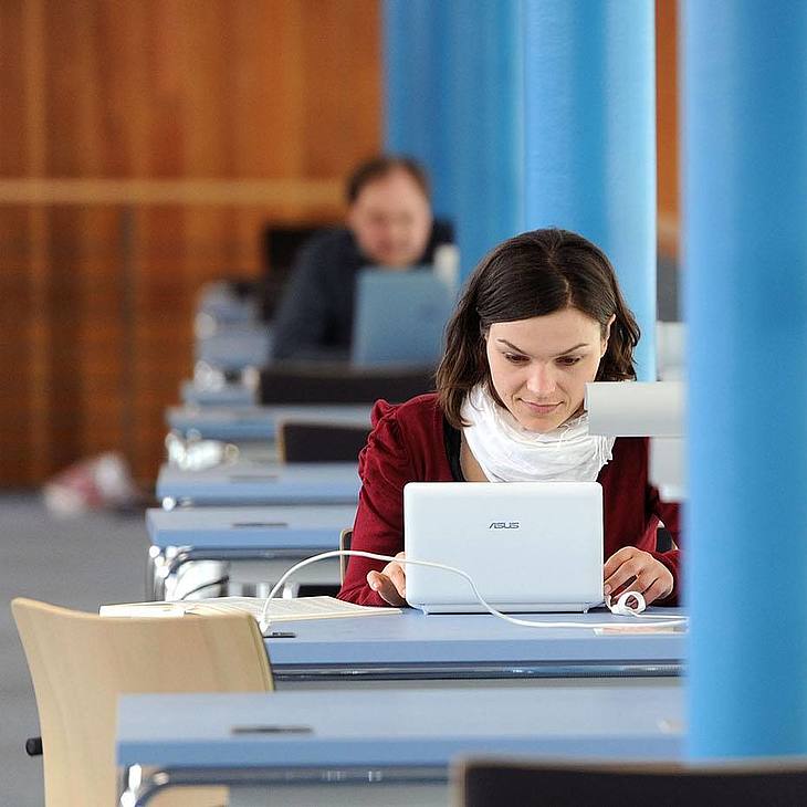 Studentin arbeitet mit ihrem Laptop an einem Schreibtisch in der Bibliothek