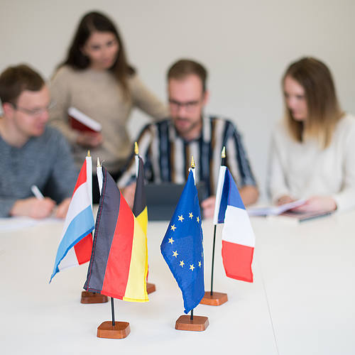 Europa-Fahnen auf einem Tisch im Vordergrund, im Hintergrund vier junge Leute.