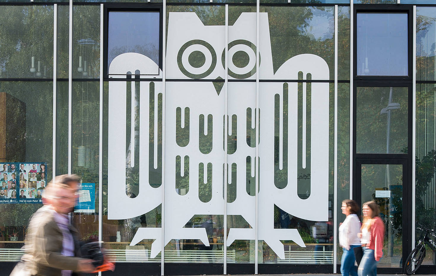 Ausschnitt eines Glasbaus mit großem weißen Logo der Universität des Saarlandes auf den Fenstern