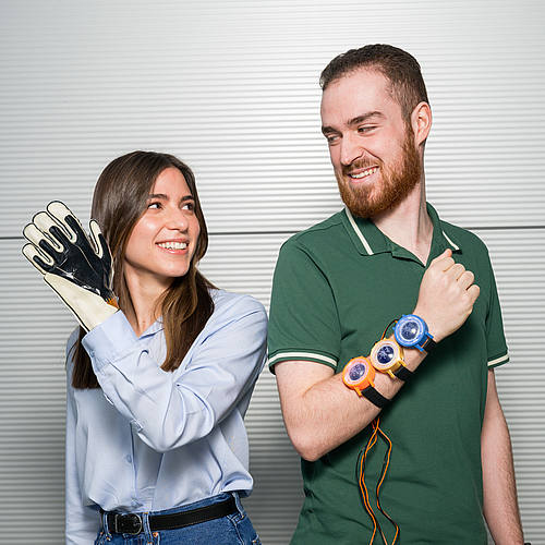 Die Doktorandin trägt einen Handschuh, in den eine smarte Folie eingearbeitet ist. Der Student neben ihr trägt drei "Uhren" mit smarten Folien auf der Rückseite am Arm.