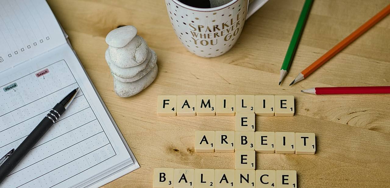 Kalender, Kugelschreiber und Buntstifte, Tasse Kaffee und aus Scrabble-Steinen die Wörter: Familie, Arbeit, Leben, Balance.