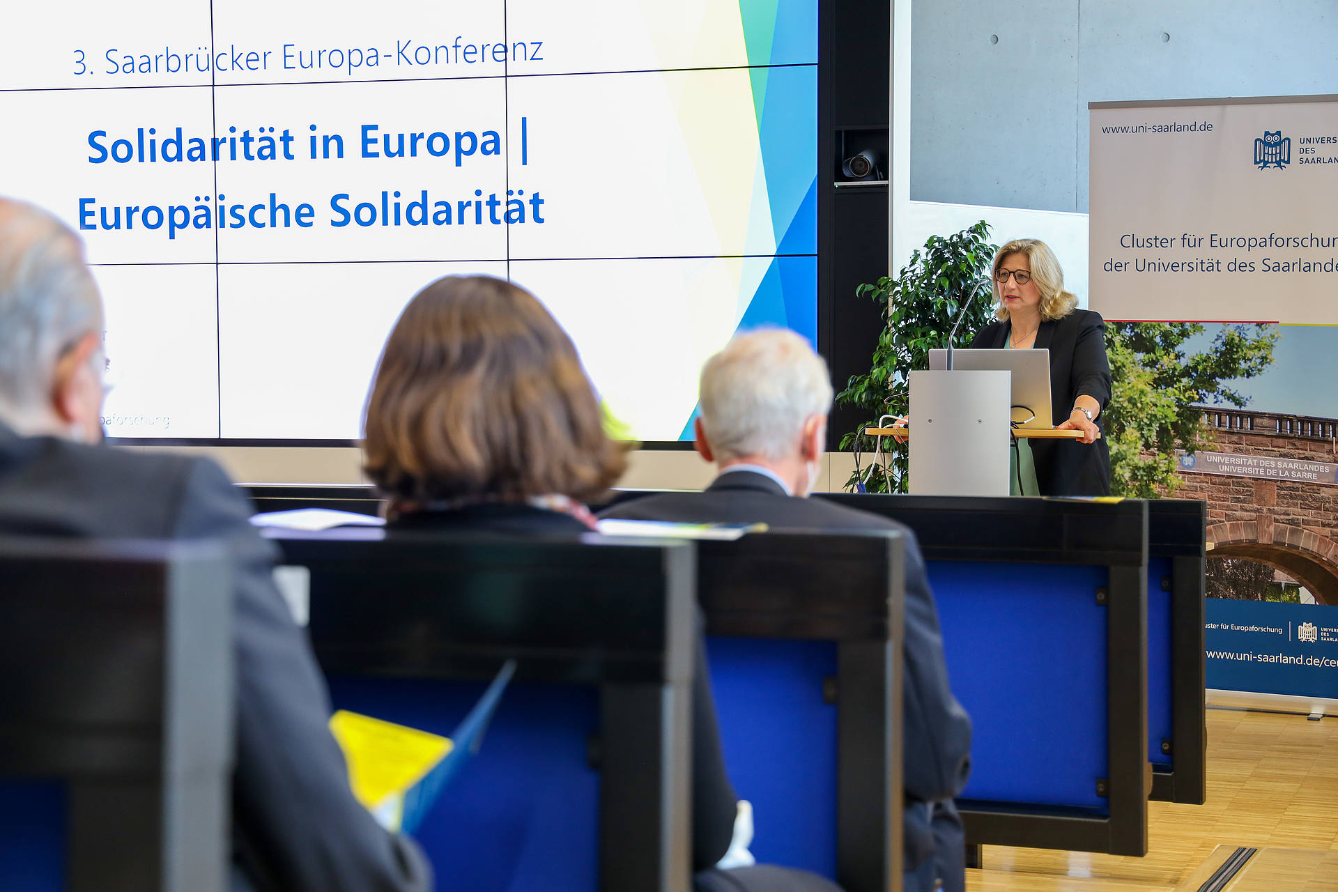 Die Ministerpräsidentin des Saarlandes, Anke Rehlinger, eröffnet die 3. Saarbrücker Europa-Konferenz mit einem Grußwort. Sie steht am Rednerinnenpult. Ein großer Bildschirm links neben ihr zeigt das Konferenzthema Solidarität in Europa, Europäische Solidarität.