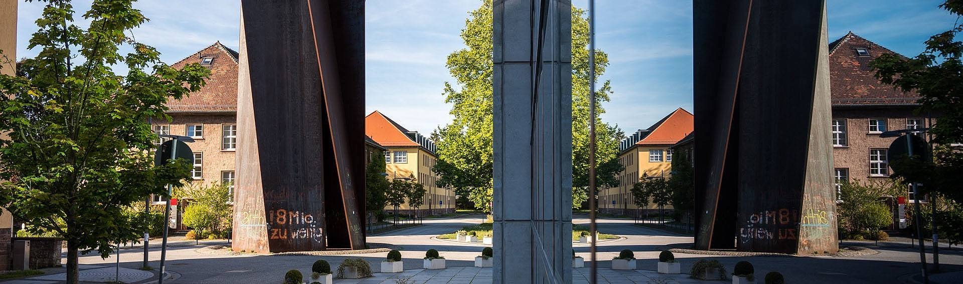 Campusansicht: Die Stahlskulptur Torque von Richard Serra gespiegelt in einer Gebäudefassade