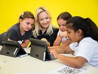 Professorin Julia Knopf bearbeitet mit drei Grundschülerinnen an einem Laptop digitale Lernmaterialien.