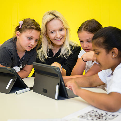 Professorin Julia Knopf bearbeitet mit drei Grundschülerinnen an einem Laptop digitale Lernmaterialien.