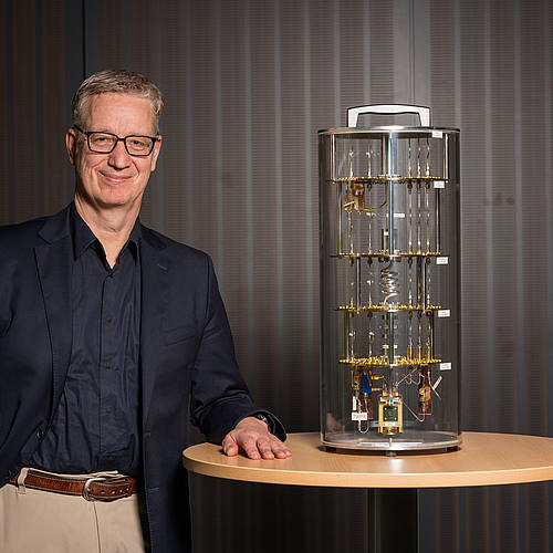 Wolfgang Maaß steht neben einem Modell eines Quantencomputers.