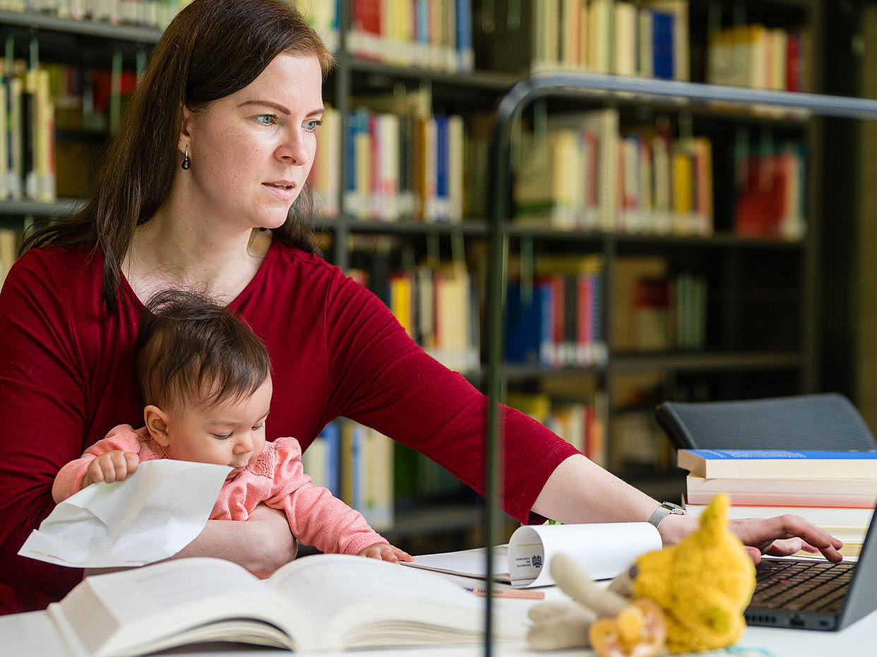 Frau an einem Tisch in der Bibliothek mit Baby auf dem Schoß