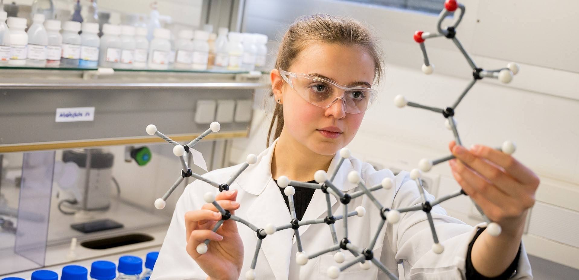 Studentin hält im Chemielabor das Modell einer chemischen Verbindung hoch