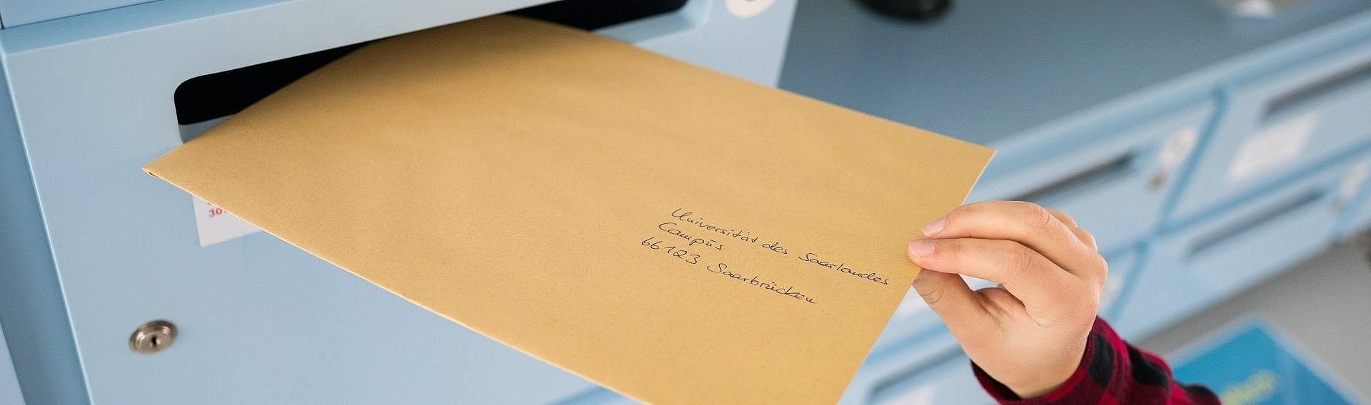 Ein an die Universität des Saarlandes adressierter Brief wird in einen Briefkasten geworfen