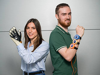 Die Doktorandin trägt einen Handschuh, in den eine smarte Folie eingearbeitet ist. Der Student neben ihr trägt am Arm drei "Uhren" mit smarten Folien auf der Rückseite.