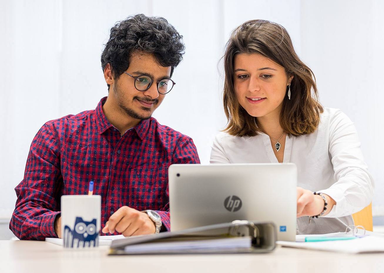 Zwei Studierende sitzen am Schreibtisch und schauen gemeinsam in einen Laptop
