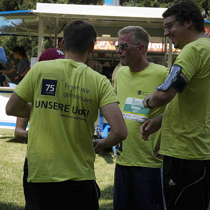 Drei Männer in gelb-grünen Universitäts-T-Shirts reden miteinander