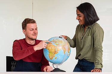 Ein junger Mann und eine junge Frau betrachten einen Globus.