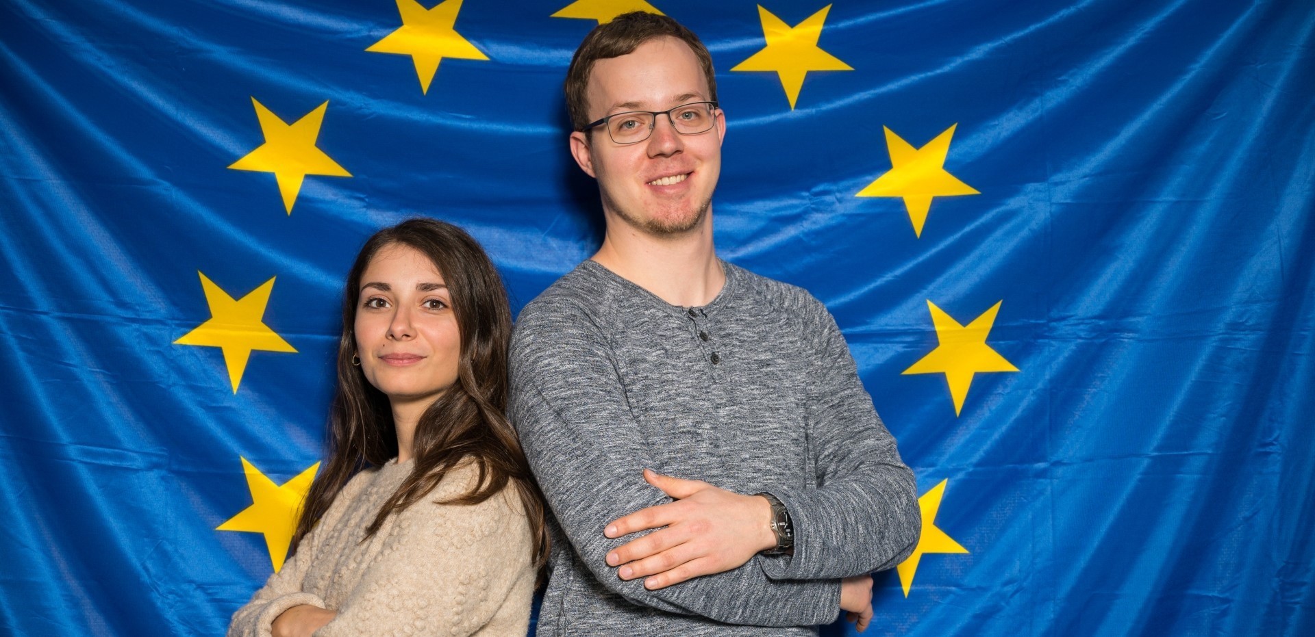 Zwei Studierende stehen vor einer Europaflagge
