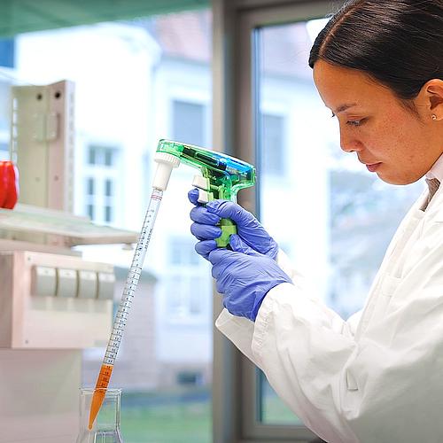 Junge Frau im Laborkittel und mit blauen Handschuhen beim Pipettieren