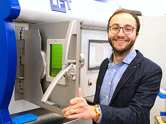 Oliver Maurer Der Forscher steht an einem 3-Drucker, an dem er gerade die Tür geöffnet hat.