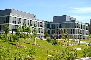 Das Forschungsgebäude (graue, moderne Fassade) mit Grünpflanzung davor.