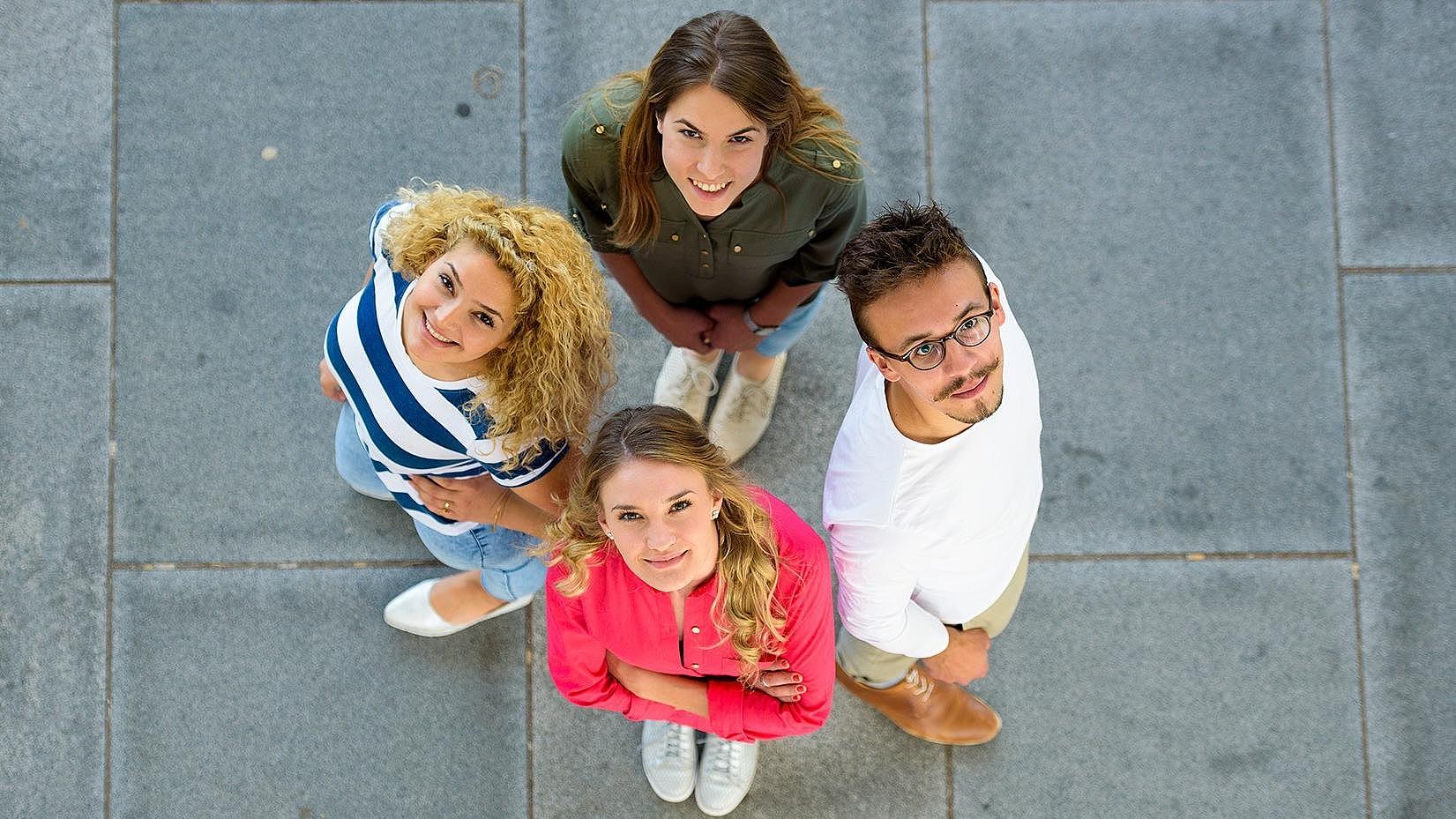 Aufsicht auf vier Studierende, die Rücken an Rücken stehen und nach oben schauen