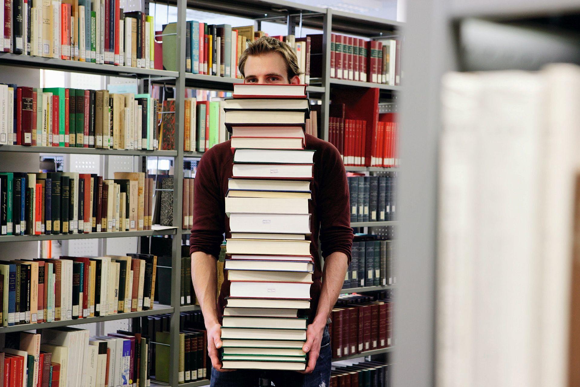 Studentin trägt viele Bücher durch eine Bibliothek