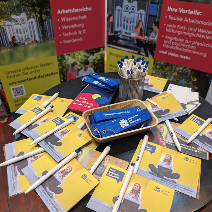 Stehtisch am Messestand, der ausgelegt ist mit Flyern, Schlüsselanhängern und Kugelschreibern.