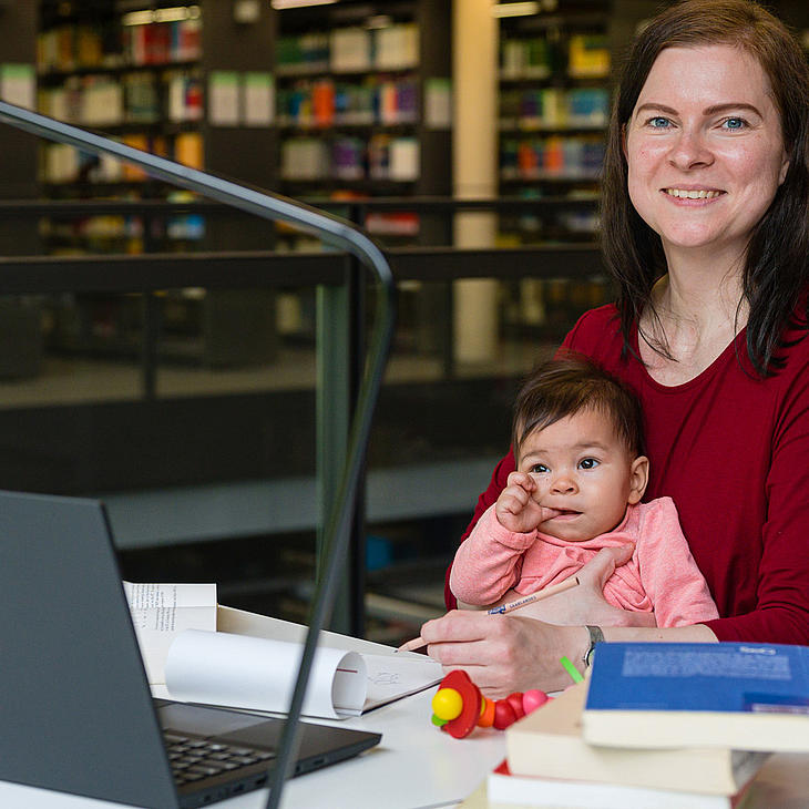 Frau an einem Tisch in der Bibliothek mit Baby auf dem Schoß